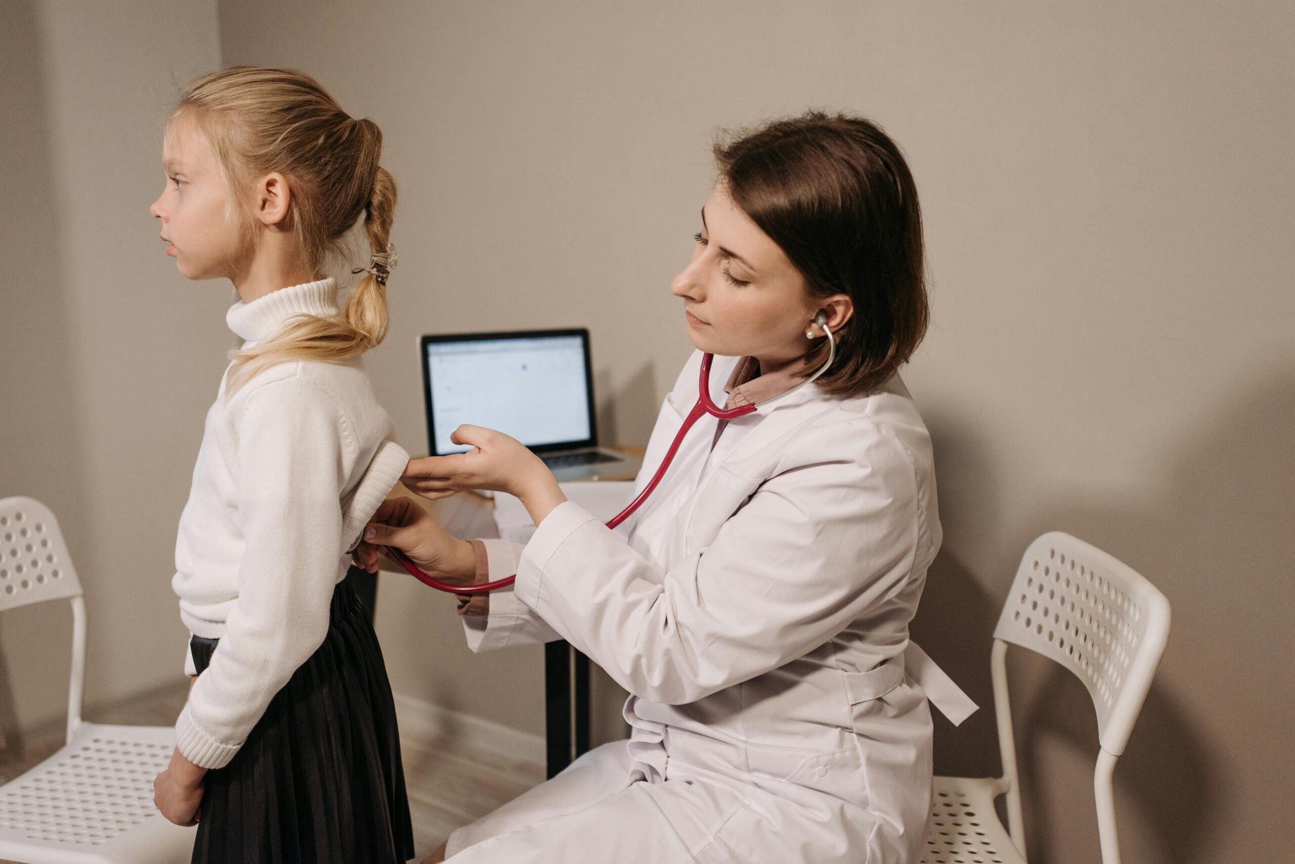 A doctor uses a stethoscope during a child's medical exam in a clinic setting.